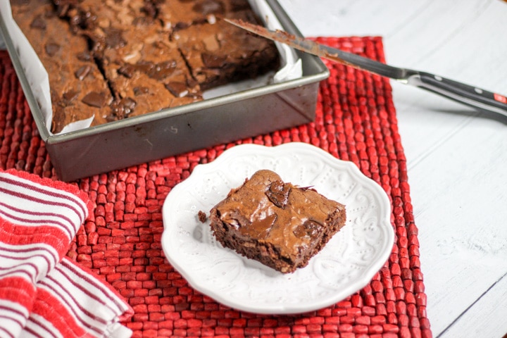 Metal sheet pan with chewy fudge brownies from scratch with one brownie on a white plate