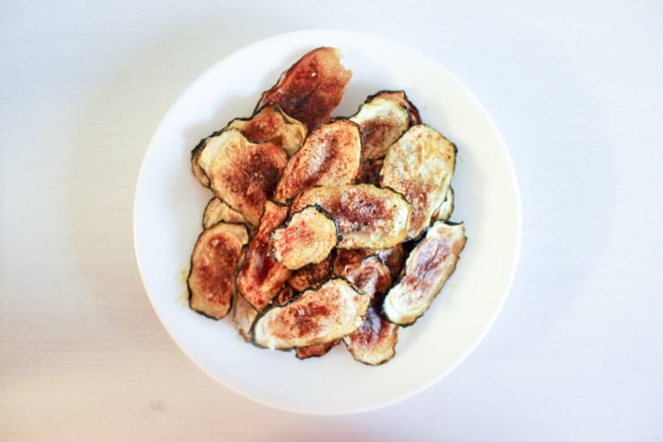 Oven baked zucchini chips seasoned with salt pepper and paprika on a white plate