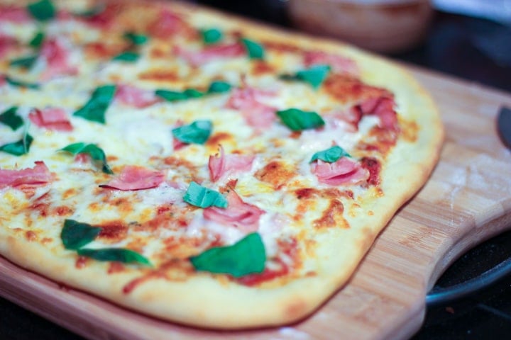 Homemade pizza made in the oven on a cutting board topped with fresh basil and mozzarella