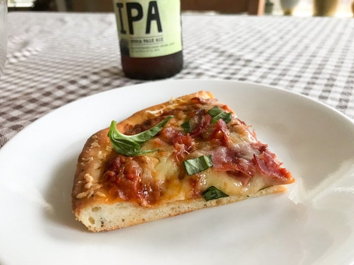 homemade pizza slice with ham cheese and basil on a plate with an IPA beer