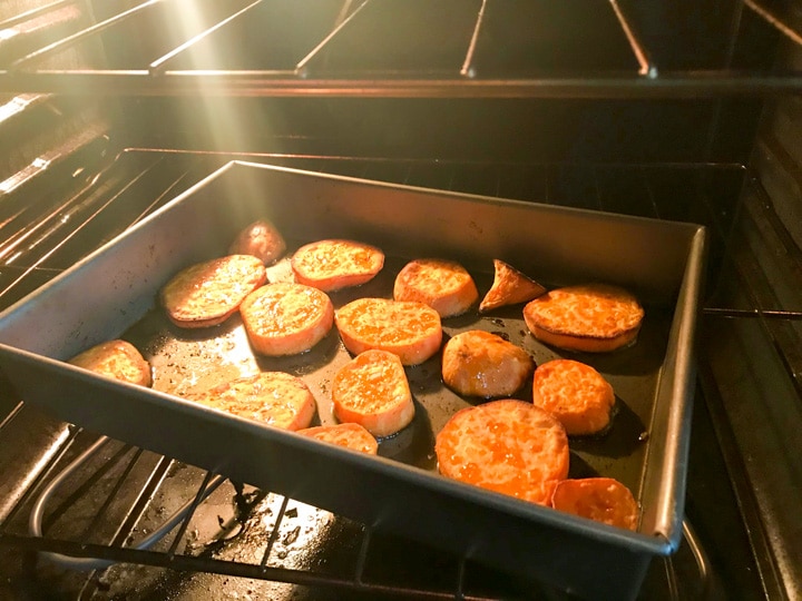 sliced sweet potatoes in a rimmed baking sheet in the oven