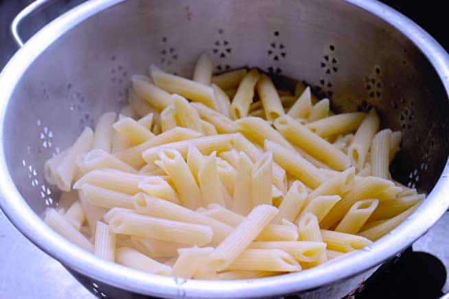 straining cooked penne pasta for pasta salad
