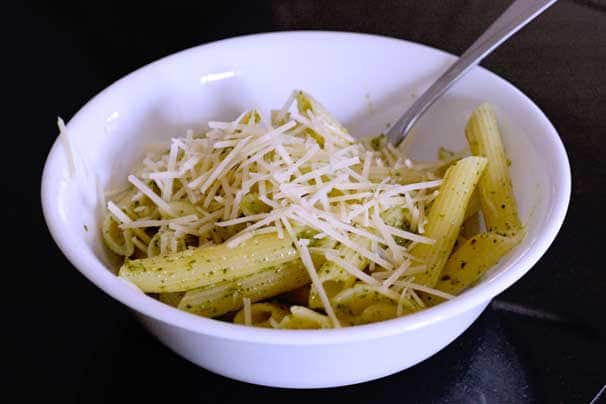 creamy pesto pasta in a salad bowl topped with Parmesan cheese