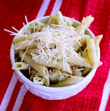 creamy pesto pasta salad in a white bowl on a red kitchen towel