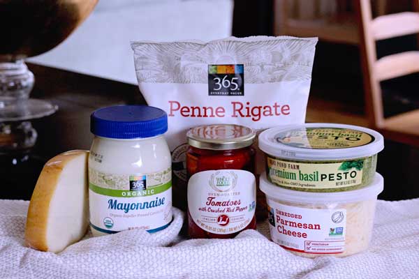 ingredients for creamy pesto pasta salad with with store bought pesto including tomatoes, mozzarella, pesto, mayo, penne pasta, parmesan cheese