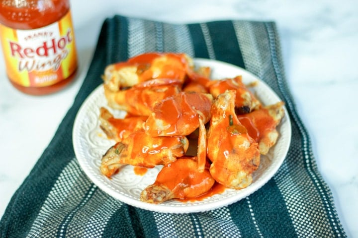 Top shot of hot wings on white plate next to bottle of hot sauce