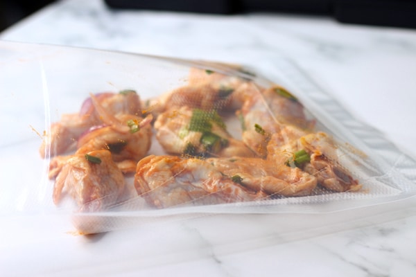 Chicken wings with hot sauce and sliced onions sitting inside plastic vacuum seal bag