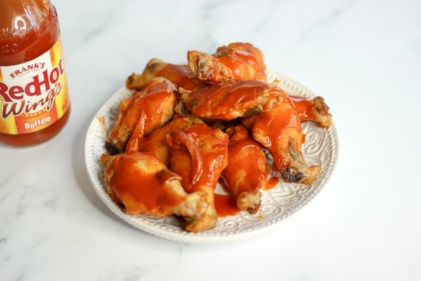 Hot wings on white plate next to bottle of hot sauce