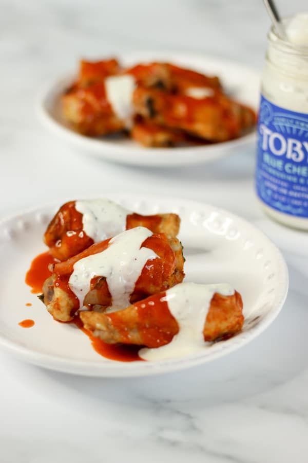 Hot wings covered in sauce and bleu cheese dressing on white plates