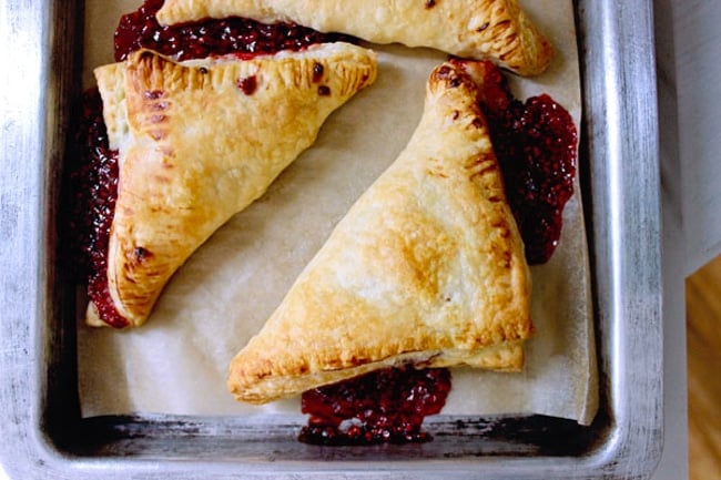 Top shot of freshly baked raspberry puff pastry turnovers baked in the oven on a sheet pan.