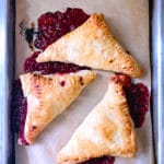 Three triangle pastries bursting with red fruit filling on sheet pan.