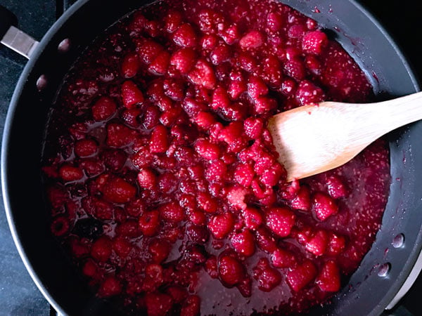 Top shot of raspberries cooking in skillet with wooden spoon.