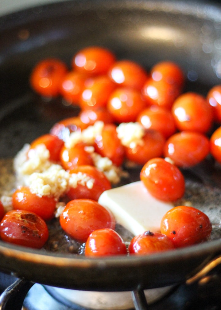 roasting pan with cherry tomatoes, garlic and butter on the stove