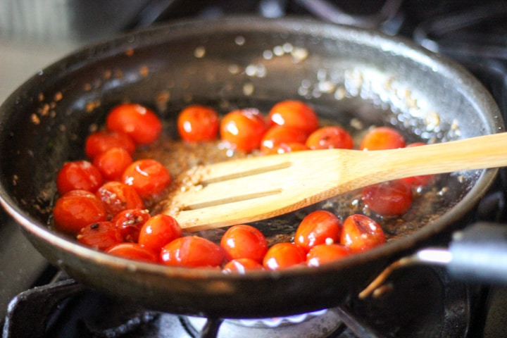 action shot of how to roast cherry tomatoes with garlic on the stove