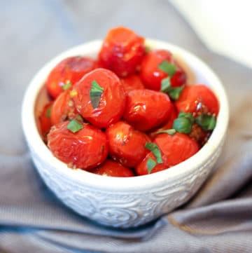 roasted cherry tomatoes with garlic in a white dish with basil
