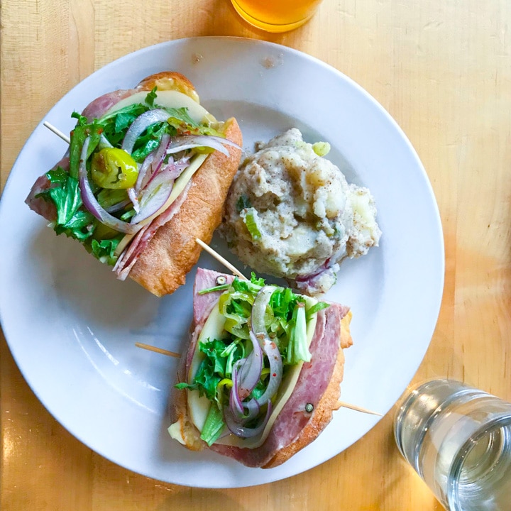 olympia provisions lunch menu item italian sandwich on a table with beer in portland