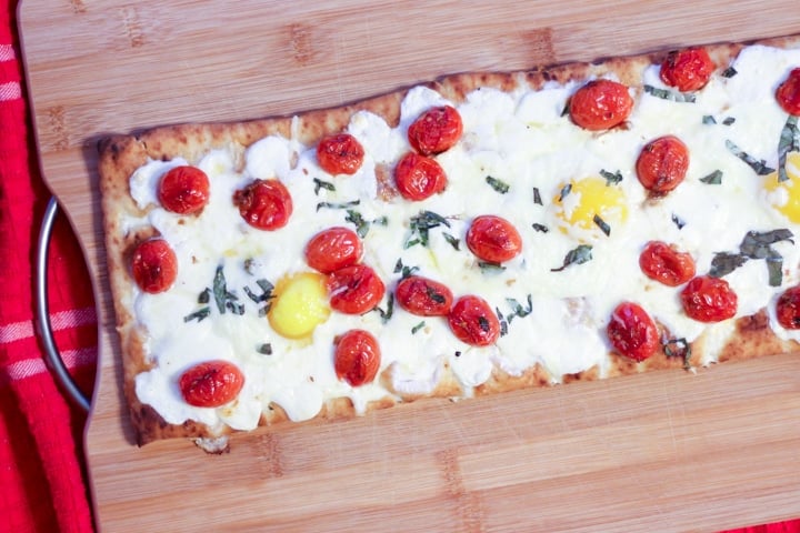 Baked breakfast pizza with eggs and tomatoes on a cutting board