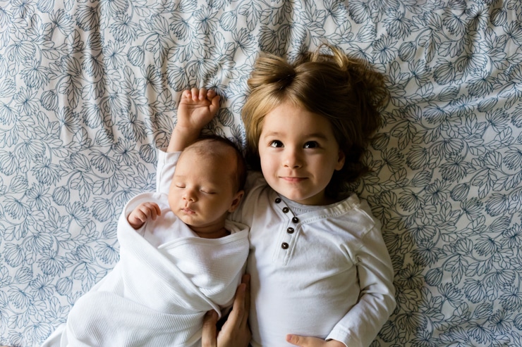 Baby sleeping in white swaddle next to a sister