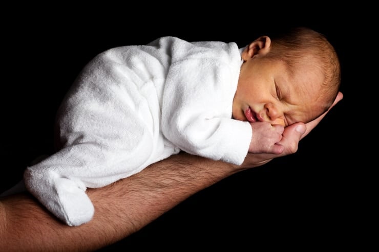 Baby sleeping in a long sleeve footed fleece pajamas while being held