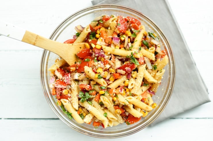 overhead process shot of Mexican pasta salad with chili lime dressing in a large glass bowl with gray napkin