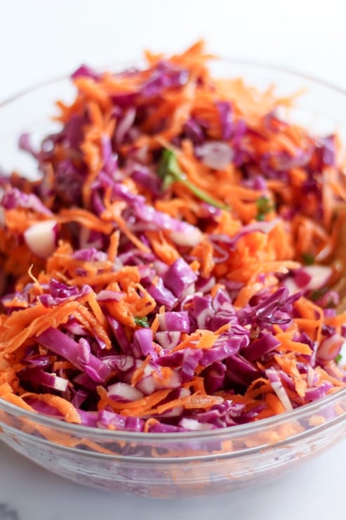 Close up shot of shredded cabbage and carrot slaw in glass mixing bowl.