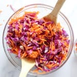 shredded carrots and shredded red cabbage with a no vinegar dressing in a glass bowl with wood spoons