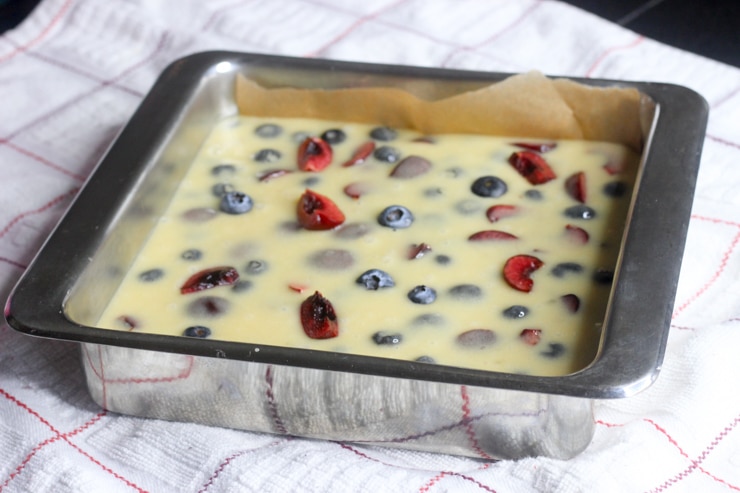 cake bar batter with fresh blueberries and cherries in a baking pan