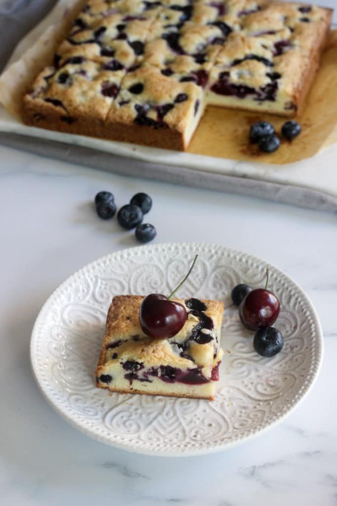 serving fresh blueberry and cherry cake bars on a white plate