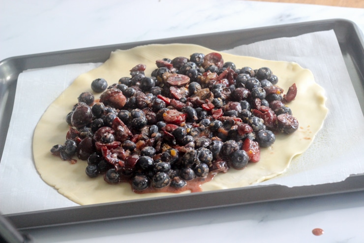 Adding mixed berry galette filling to the pie crust on a baking sheet