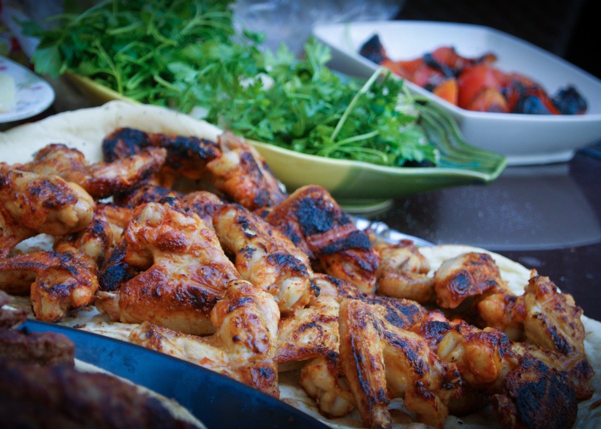 Grilled chicken wings on white plate next to bowl of cilantro