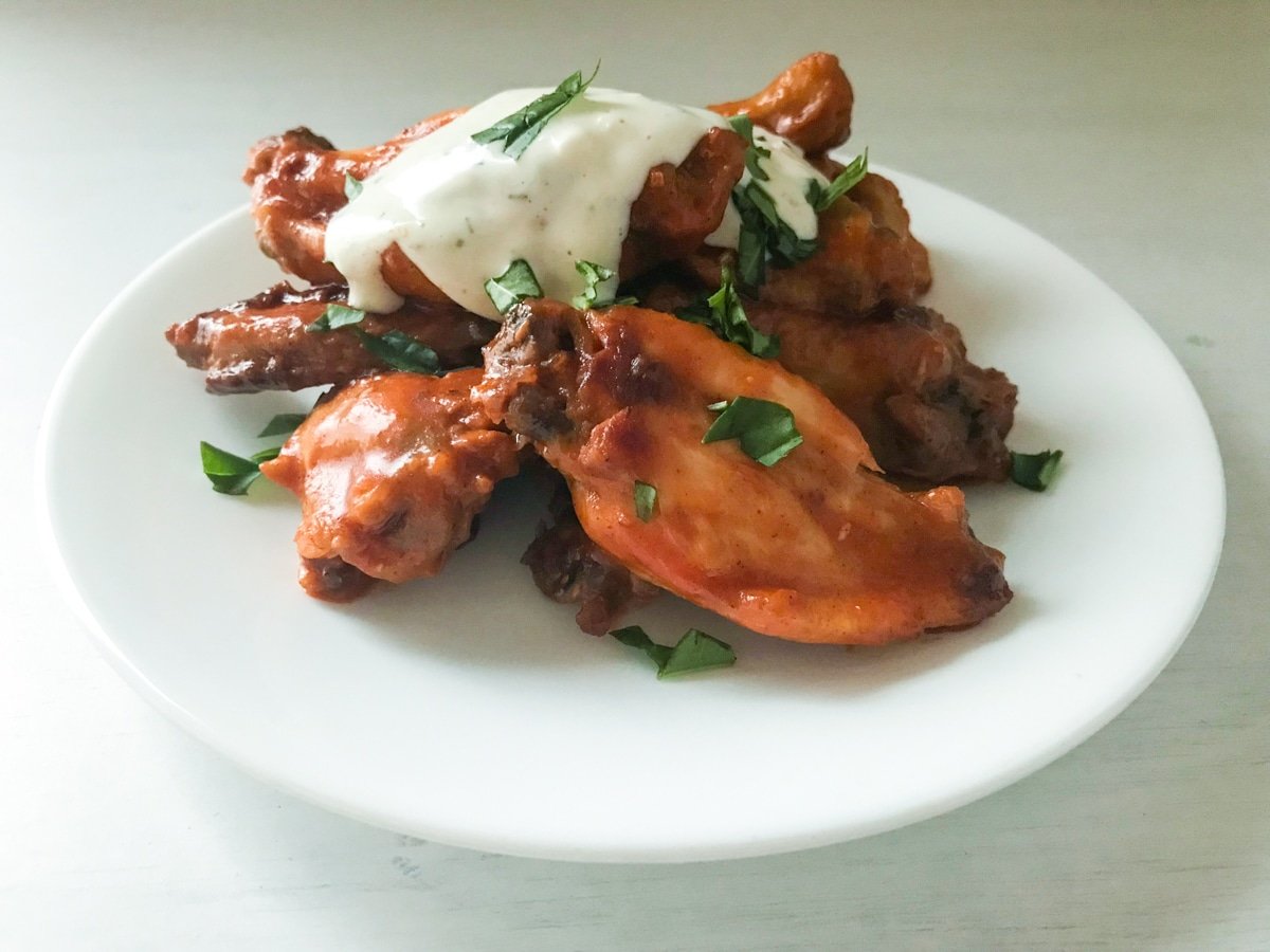 Hot wings covered in sauce and bleu cheese dressing on white plate