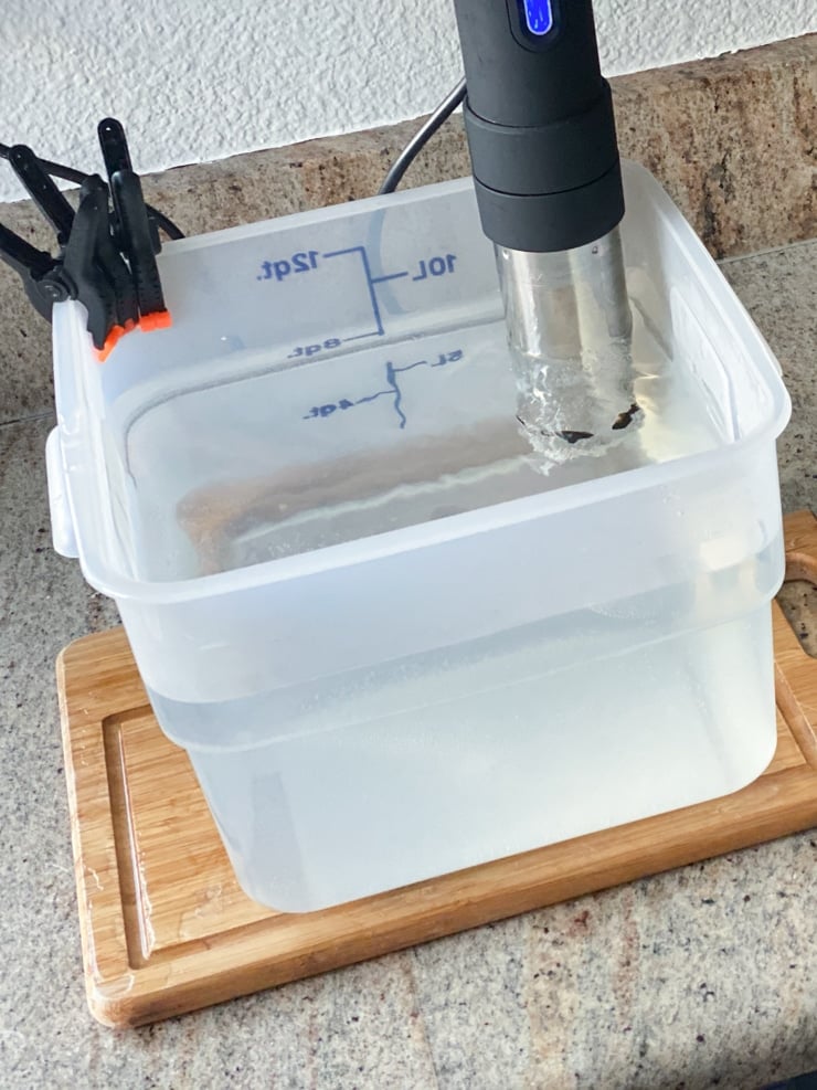 sous vide water bath in a plastic container on a cutting board