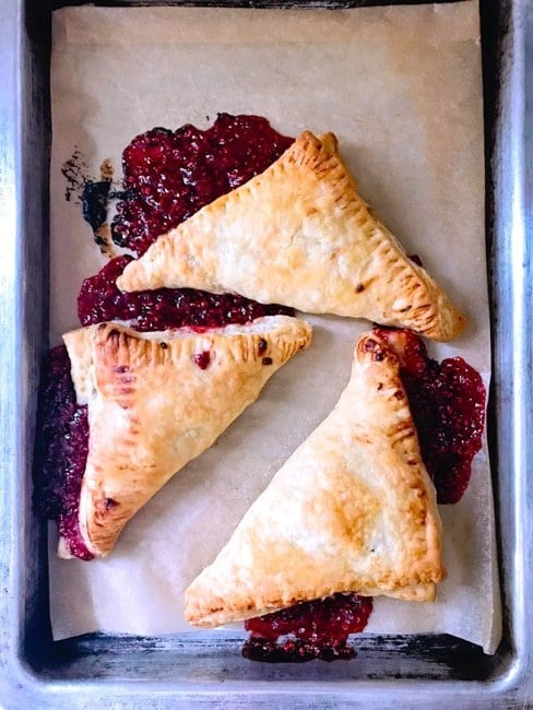 Top shot of freshly baked raspberry puff pastry turnovers baked in the oven on a sheet pan.