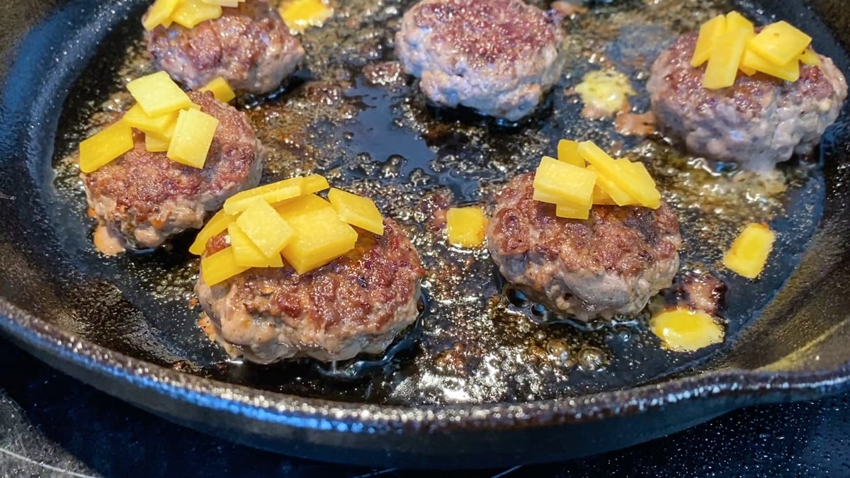 mini ground beef patties cooking in cast iron skillet
