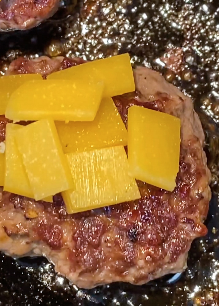 hamburger searing in a cast iron skillet with mayo and cheese