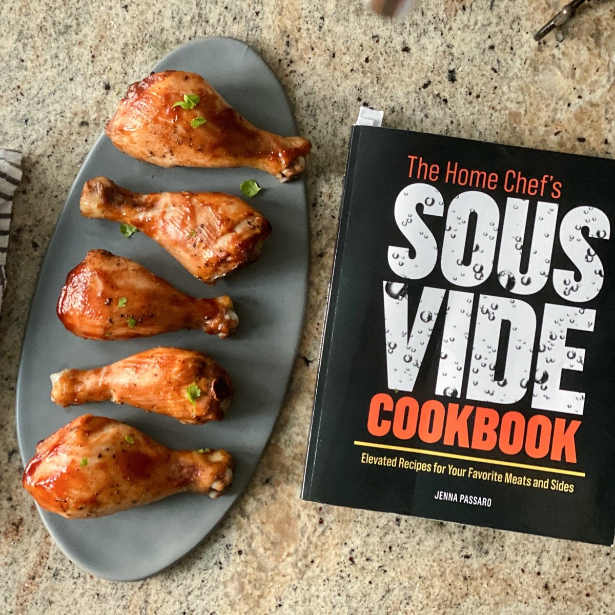 Cooked chicken legs on gray oval plate next to cookbook