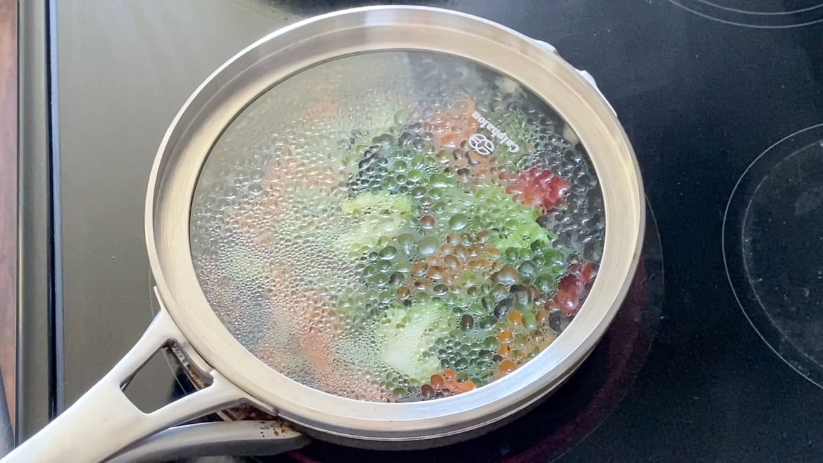 steaming vegetables in a pan on the stove with water and a pot cover