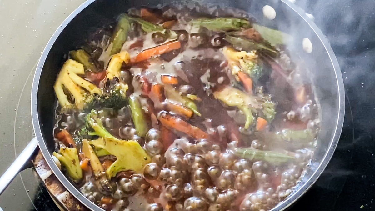 Asian sauce packet bubbling in stir fry with frozen vegetables