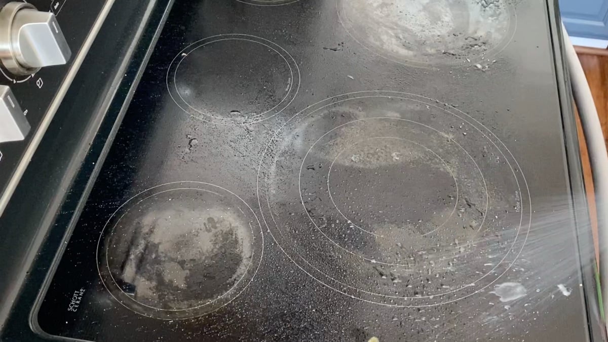 Spraying black stovetop with kitchen cleaner.