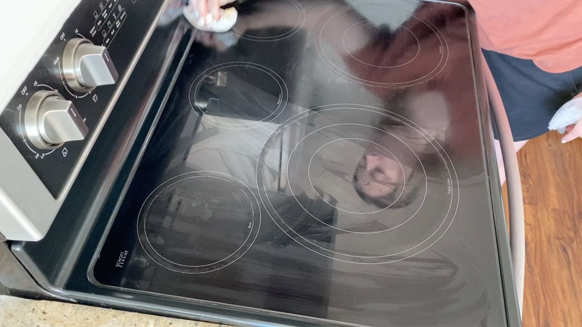 Using a clean wet paper towel to clean a stove top.