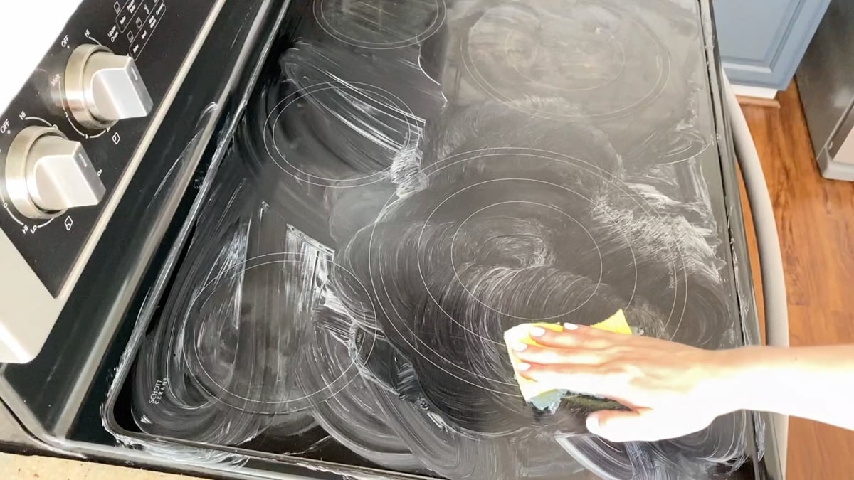 Scrubbing flat stove top with a sponge.