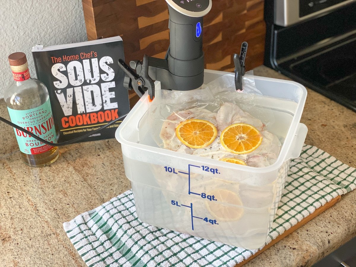 Protein vacuum sealed with orange slices sitting in bucket filled with water.