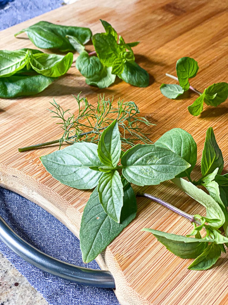 cutting board with fresh herbs for cooking including Thai basil dill and thyme