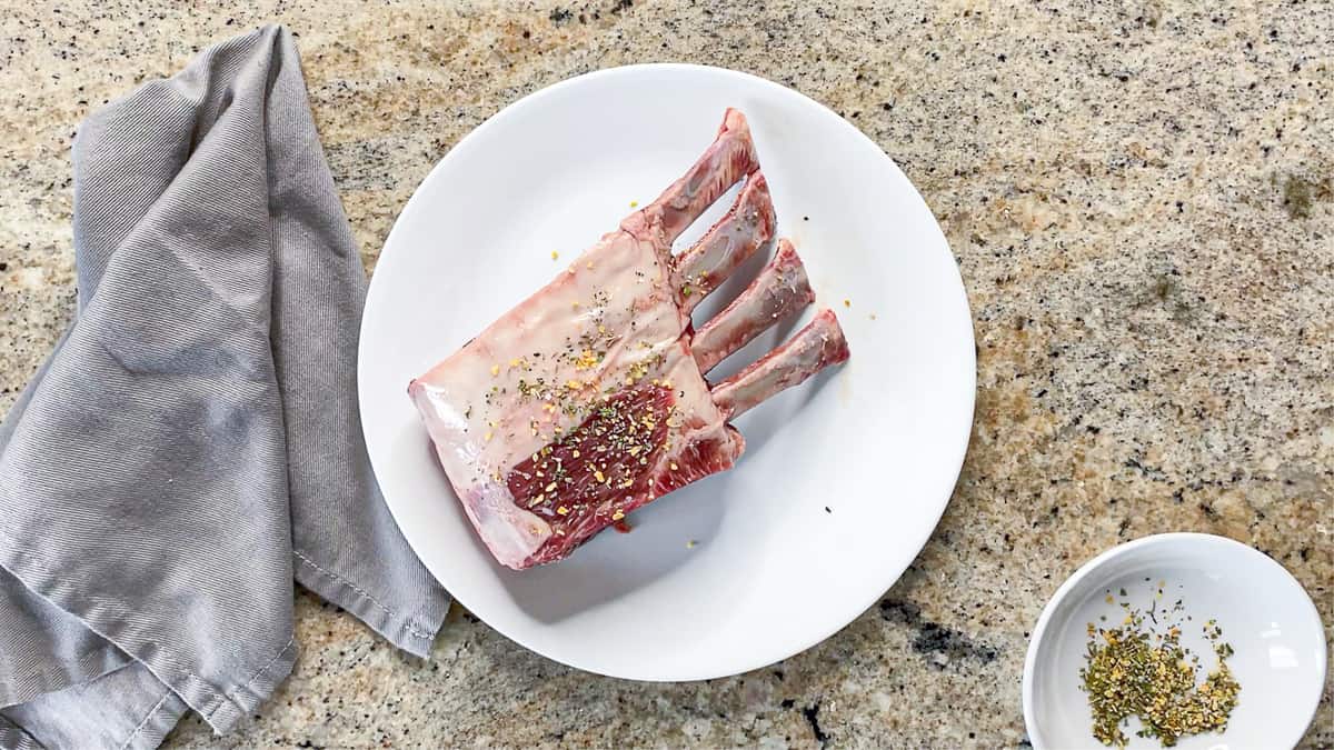top shot of seasoned meat on white plate next to gray napkin on countertop