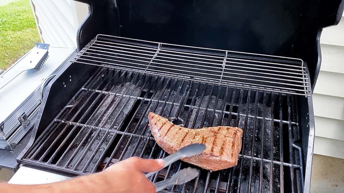 top shot of person cooking steak on grill outside with tongs