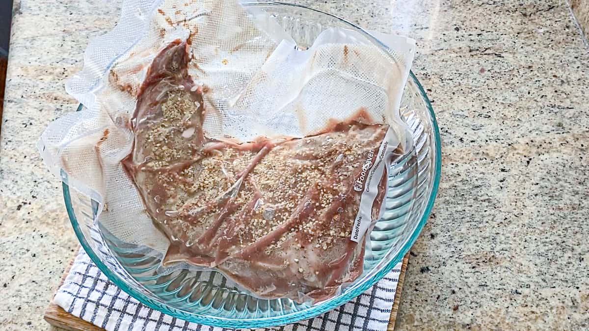 seasoned steak in vacuum sealed bag in ice bath in clear bowl