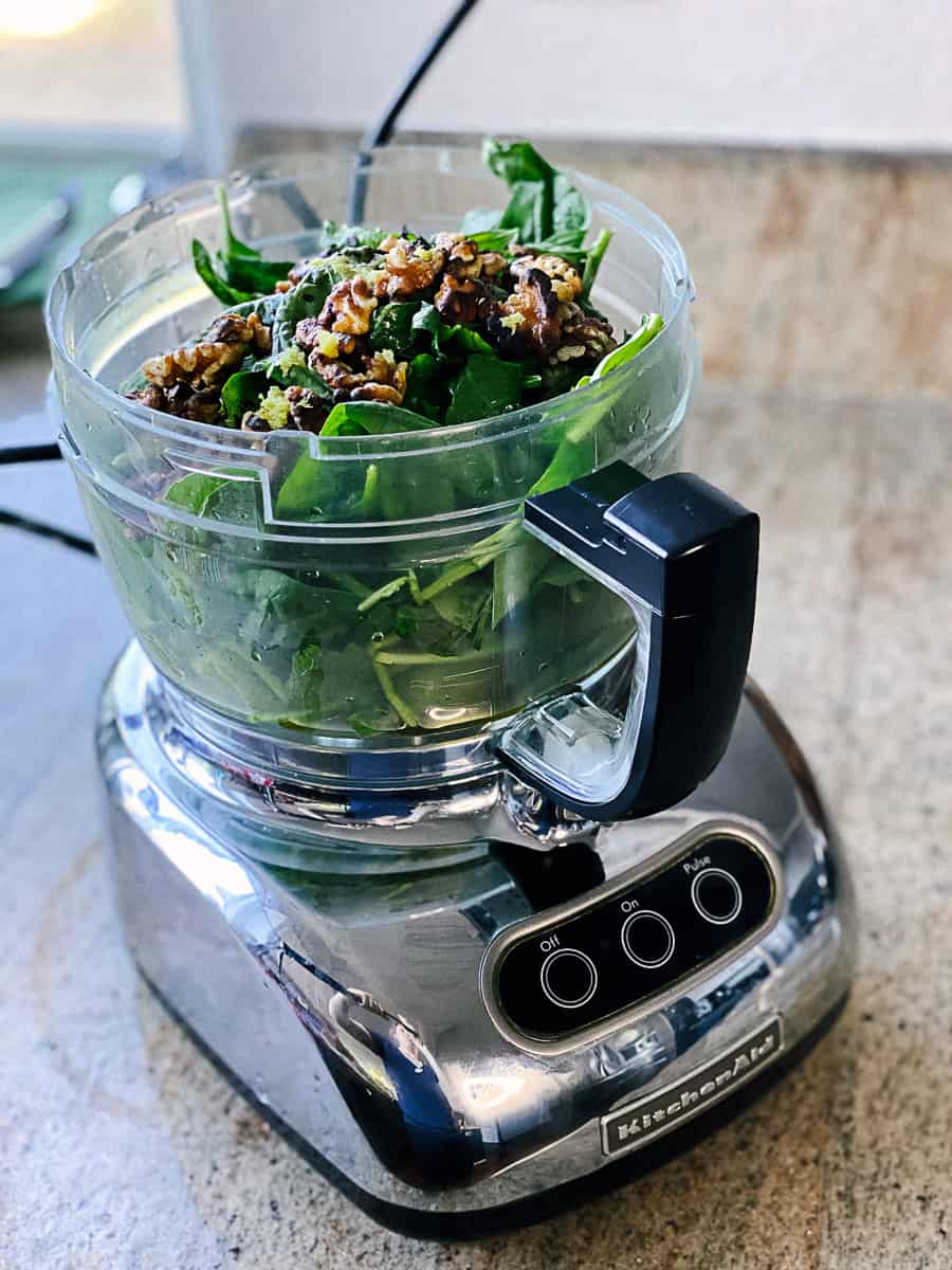 Spinach leaves, basil leaves, and chopped walnuts in food processor before blending