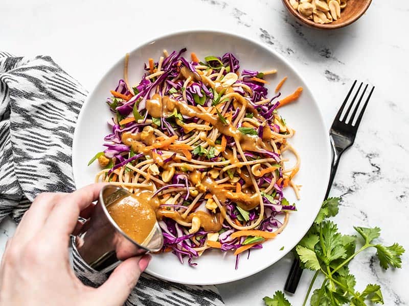 hand pouring sauce on side dish on a plate with a fork