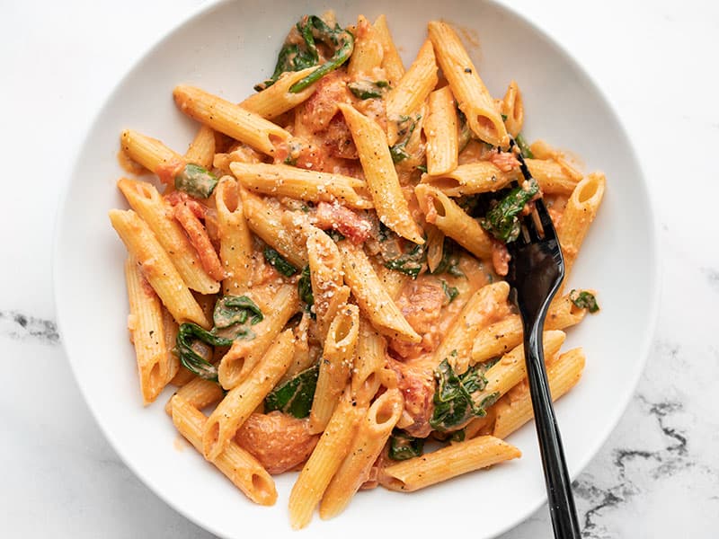 close up of creamy spinach tomato pasta bowl with fork