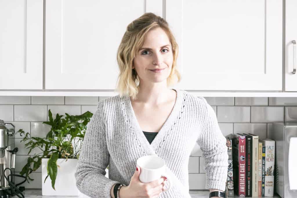 woman standing in kitchen, smiling with a mug in her hand